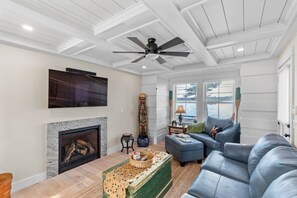 A living room with a fireplace, a ceiling fan, a television, and a large window overlooking a body of water.