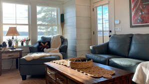 A cozy living room with a dark blue sofa, a wooden coffee table, and a window with a view of trees. - Lady of The Lake (Laconia)