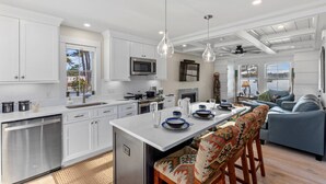 A modern kitchen with white cabinetry, a central island, pendant lighting, and a view of a snowy landscape through large windows. - Lady of The Lake (Laconia)