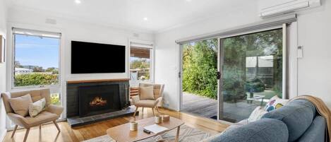 A modern living room with a fireplace, a flat-screen TV, a sofa, and a large sliding glass door leading to a balcony.