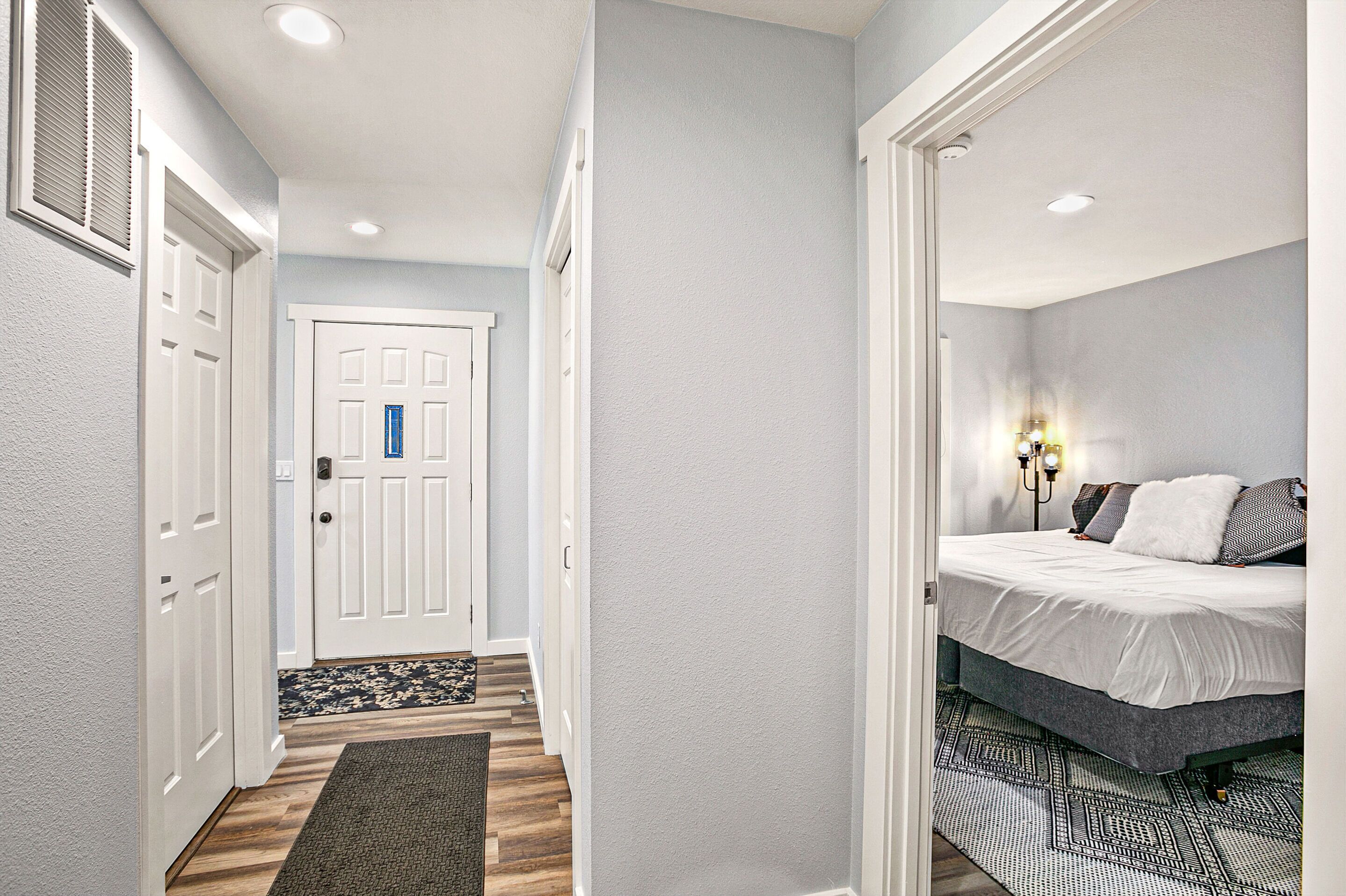 A bedroom with a bed, a nightstand, a wall-mounted lamp, and a door with a blue lock.