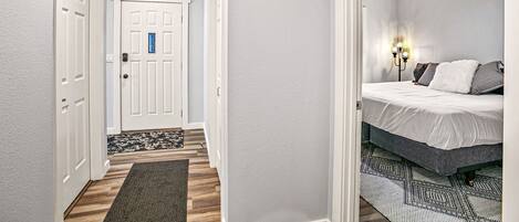 A bedroom with a bed, a nightstand, a wall-mounted lamp, and a door with a blue lock.