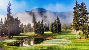 Un campo da golf con uno stagno, circondato da alberi alti e una montagna sullo sfondo.