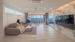 A modern living room with a large TV, a sofa, a hanging chair, and a view of the sea.
