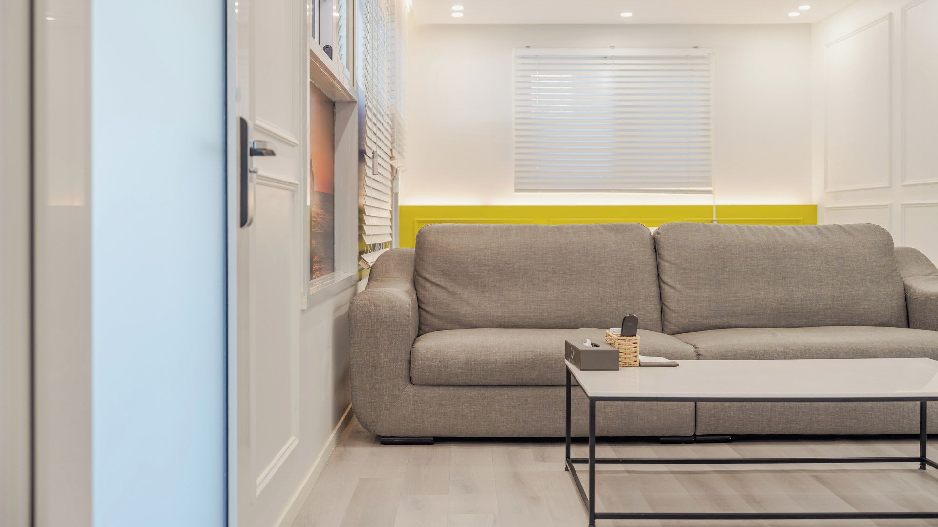 A modern living room with a grey sofa, a small table, and a window with blinds.