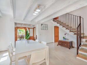 Een ruime eethoek met een witte tafel en stoelen, een houten bank met een vaas, en een trap met een leuning.