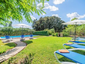 A poolside area with lounge chairs and umbrellas, surrounded by greenery and a clear sky. - Can Camarroja by Sunvillas Mallorca (Pollença)