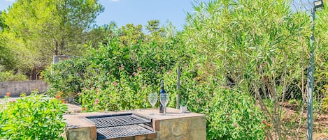 An outdoor barbecue area with a stone structure, two wine glasses, and a bottle.