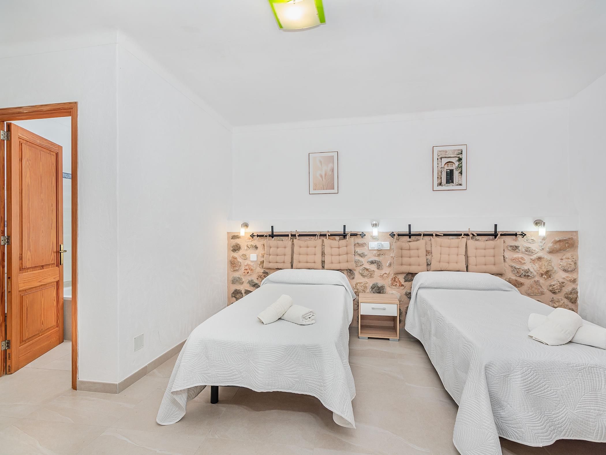 A hotel room with two single beds, a wooden door, a stone wall, and a small bedside table.