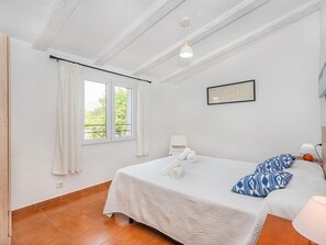 Een slaapkamer met een bed, een raam met gordijnen, een lijst met een afbeelding aan de muur en een lamp op het nachtkastje.