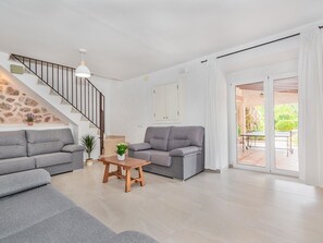 A modern living room with a staircase, grey sofas, a wooden coffee table, and a view of the outdoor patio. - Can Camarroja by Sunvillas Mallorca (Pollença)