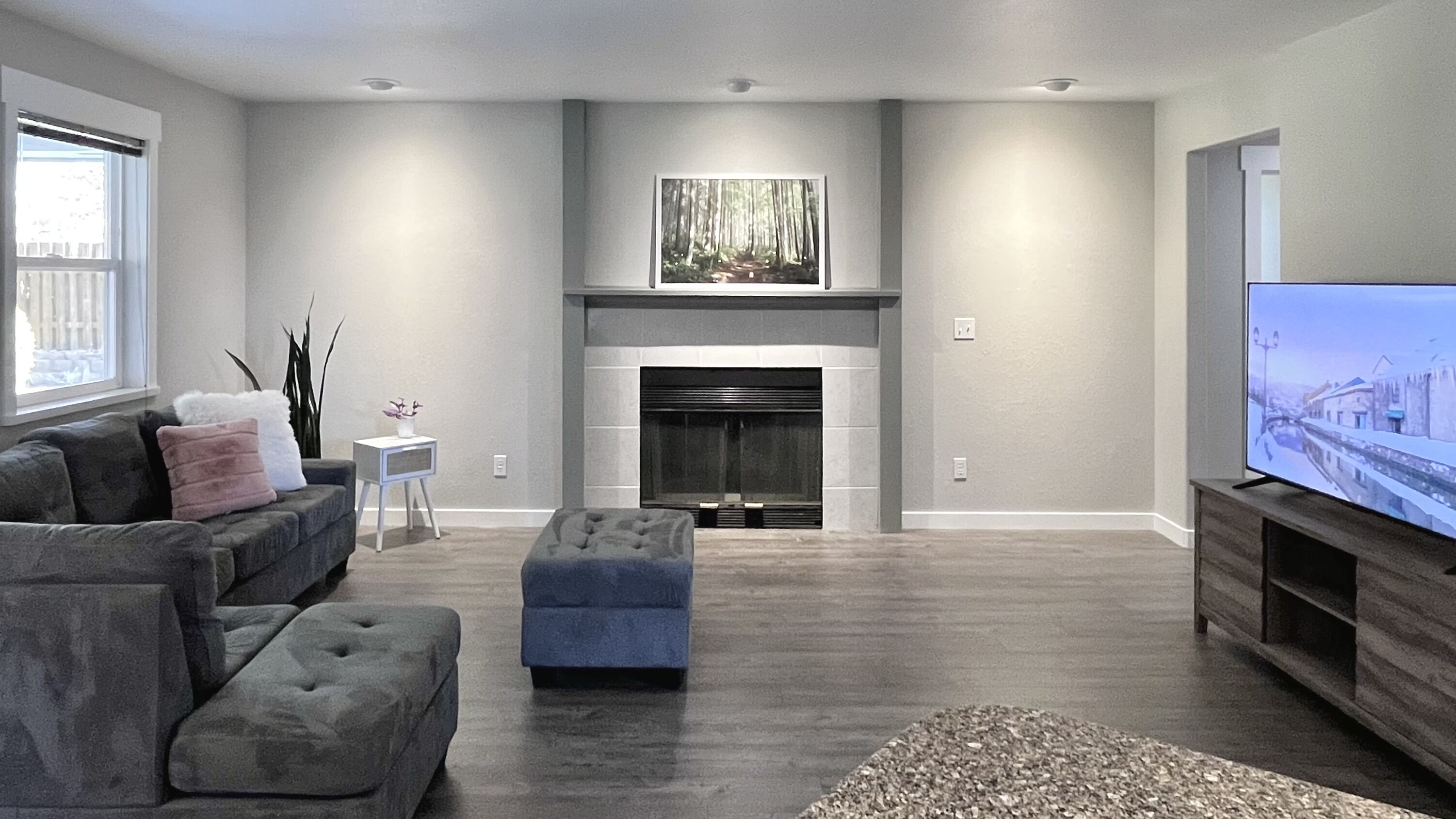Una sala de estar moderna con chimenea, sofás grises, un televisor y un ventanal grande.