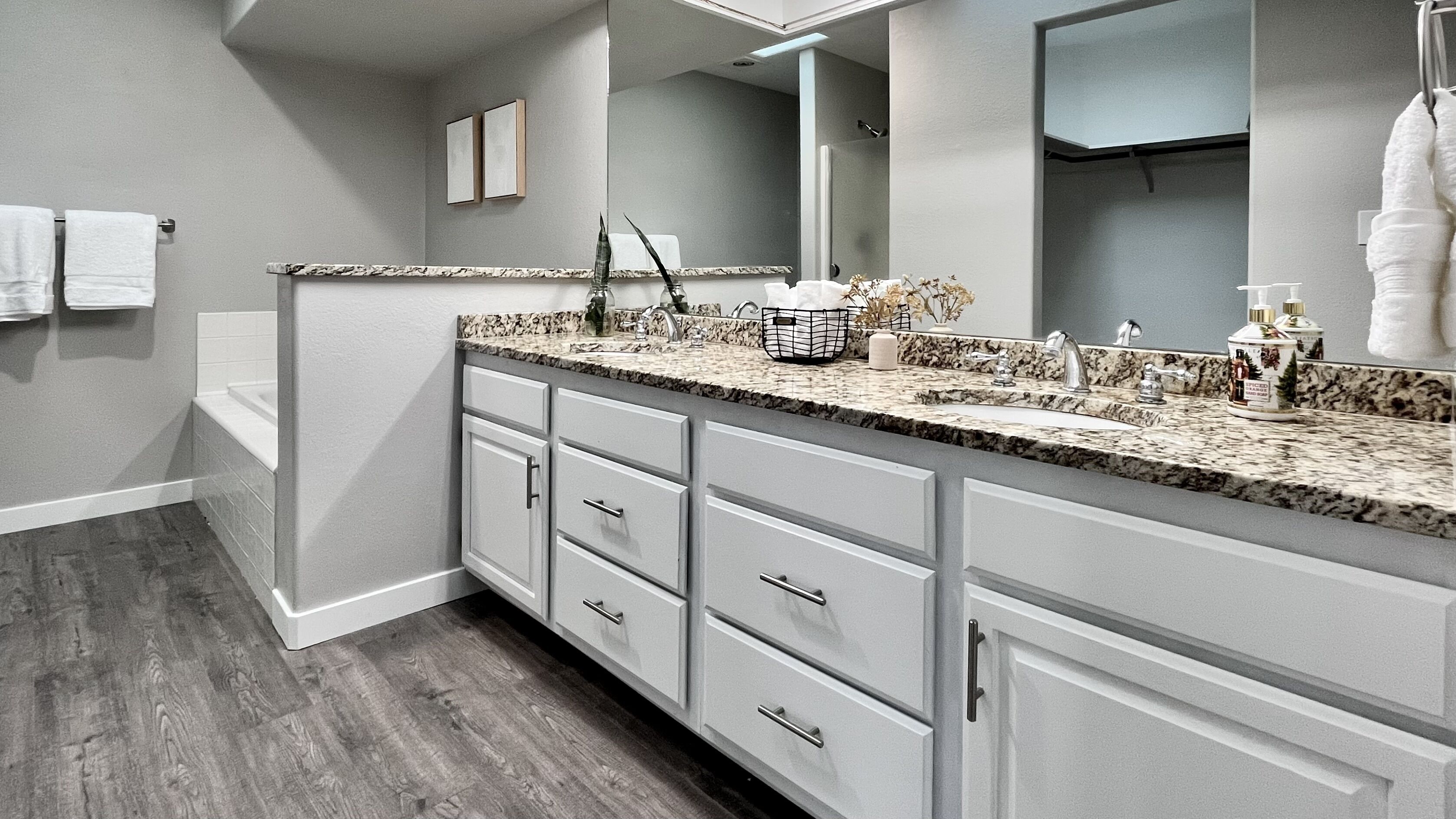 Un baño moderno con encimera de granito, lavamanos doble y muebles de color blanco.