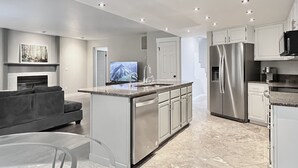A modern kitchen with stainless steel appliances, a central island with a sink, and a flat-screen TV. - Hot tub + Bright and spacious home + 20 min to Ski —> Sleeps 13! (East Wenatchee)