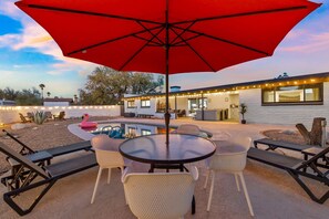 A patio with a round table, chairs, and a red umbrella. - Private Desert Oasis: Pool, HotTub, FirePit, Garage, EV Charger, Near Saguaro (Tucson)