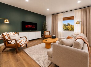 A modern living room with a sofa, armchair, coffee table, and a TV displaying 'NETFLIX'.