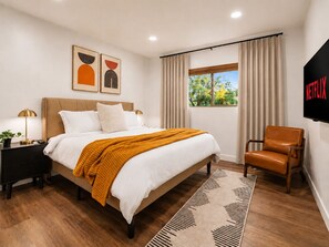 A modern bedroom with a bed, a chair, a TV, and artwork on the wall. - Private Desert Oasis: Pool, HotTub, FirePit, Garage, EV Charger, Near Saguaro (Tucson)