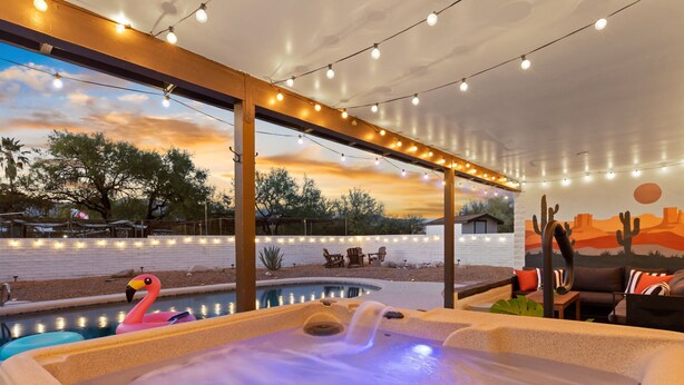 Un jacuzzi con un flotador con forma de flamenco, piscina, mobiliario exterior e iluminacion con guirnaldas.