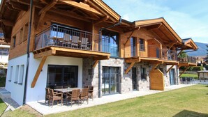 A multi-story wooden house with balconies, large windows, and a patio area with outdoor furniture. - Luxury apartment with terrace near Kaprun (Piesendorf)