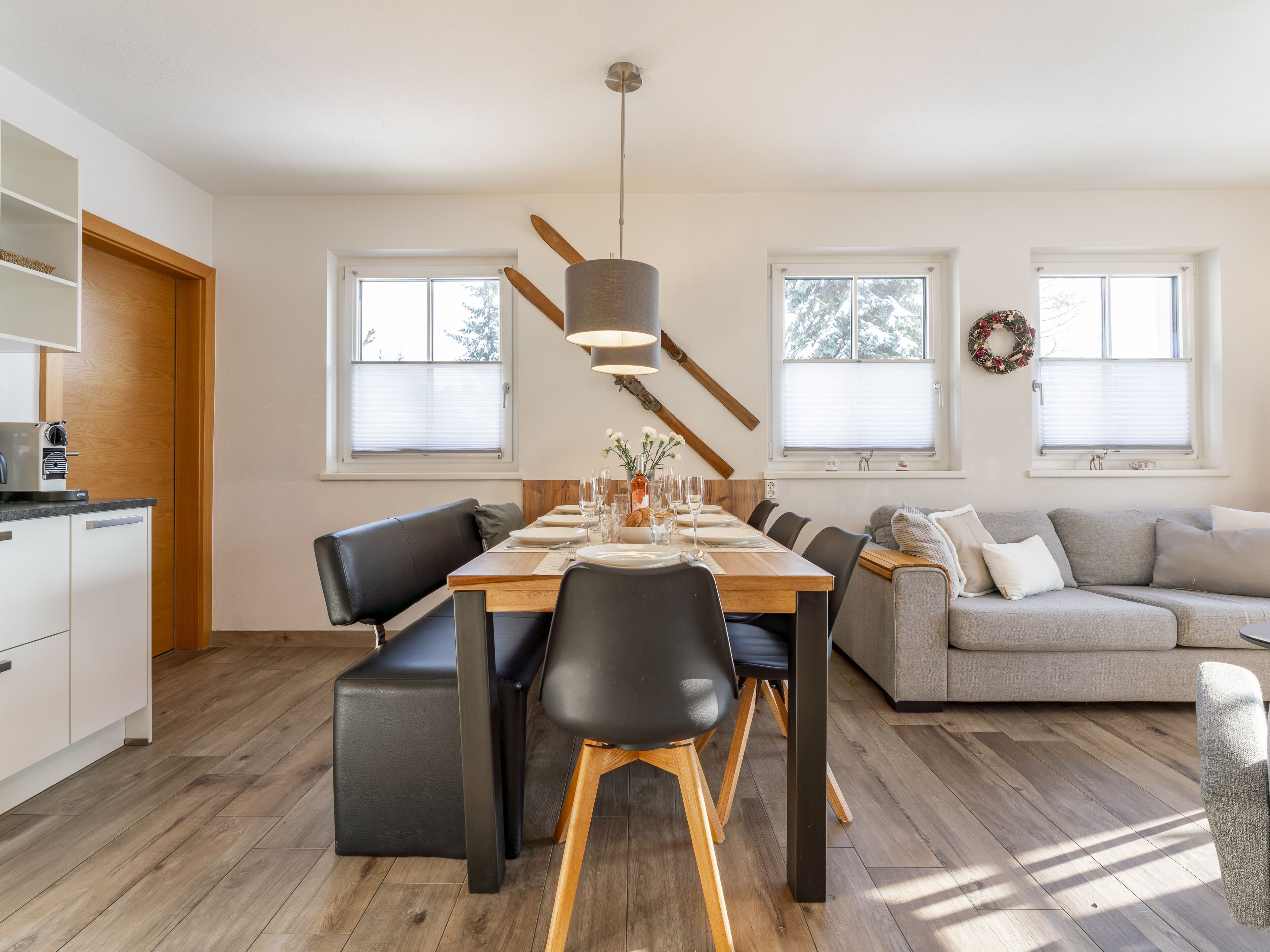Une cuisine moderne avec un coin repas, un plancher en bois et un canapé gris.