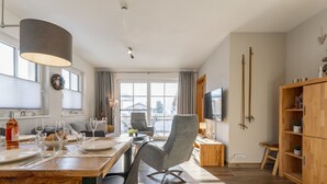A modern dining area with a wooden table, chairs, and a chandelier. There is a television on the wall and a wooden cabinet with shelves. - Luxury apartment with terrace near Kaprun (Piesendorf)