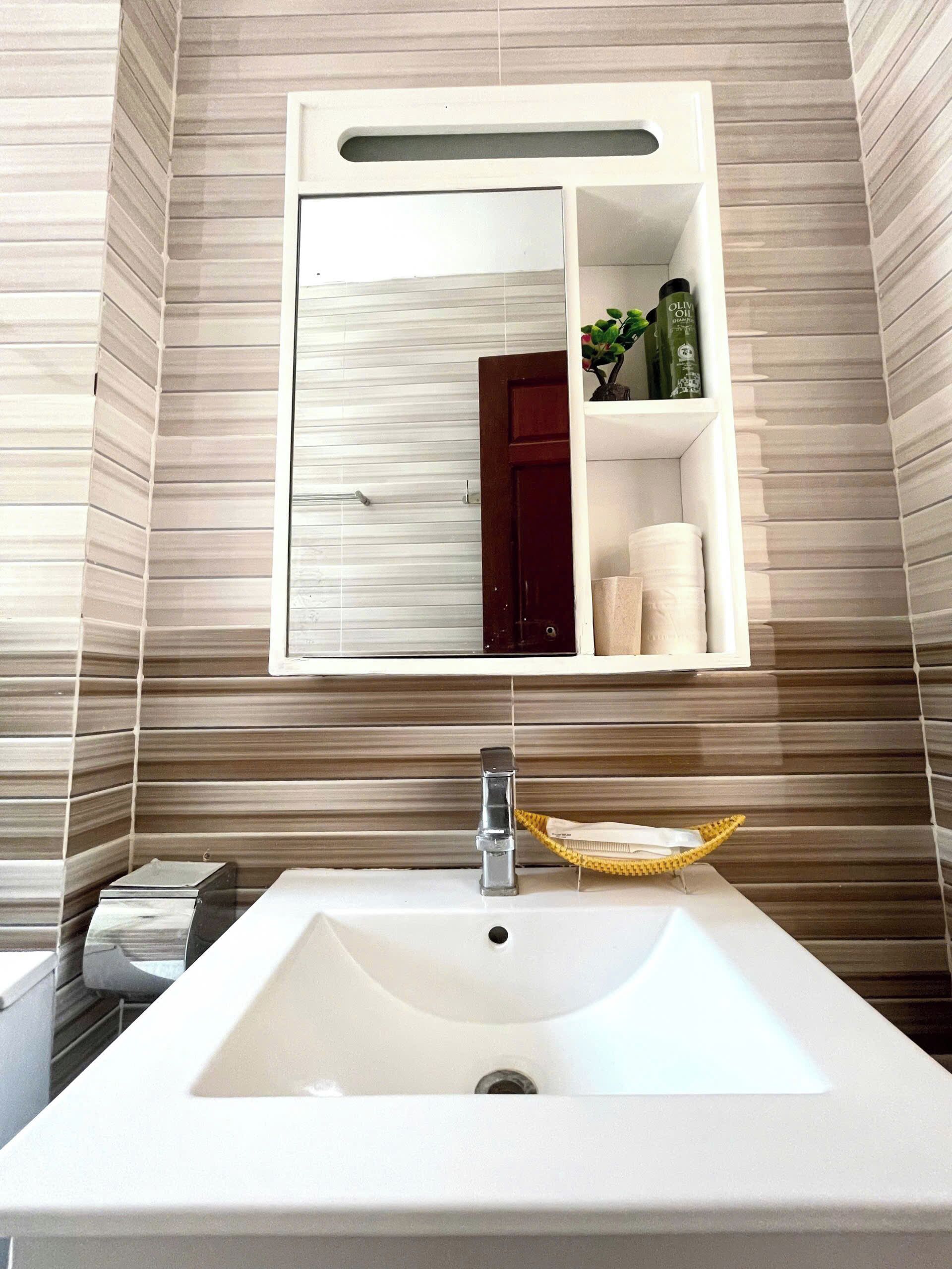 A bathroom with a white sink, a mirror, and a shelf with toiletries.
