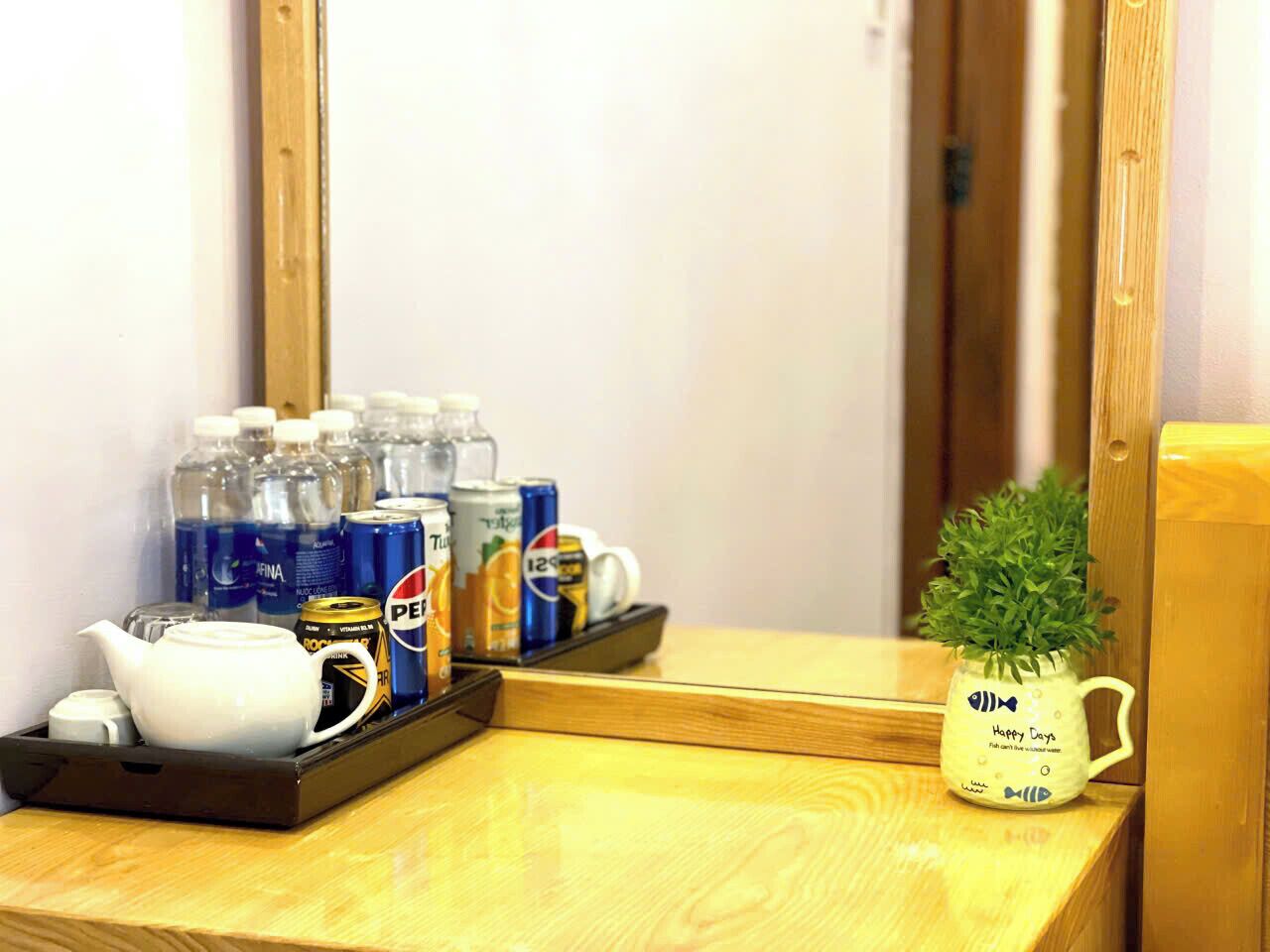 A hotel room with a wooden desk, a tray with a teapot, bottled water, and cans of Pepsi.