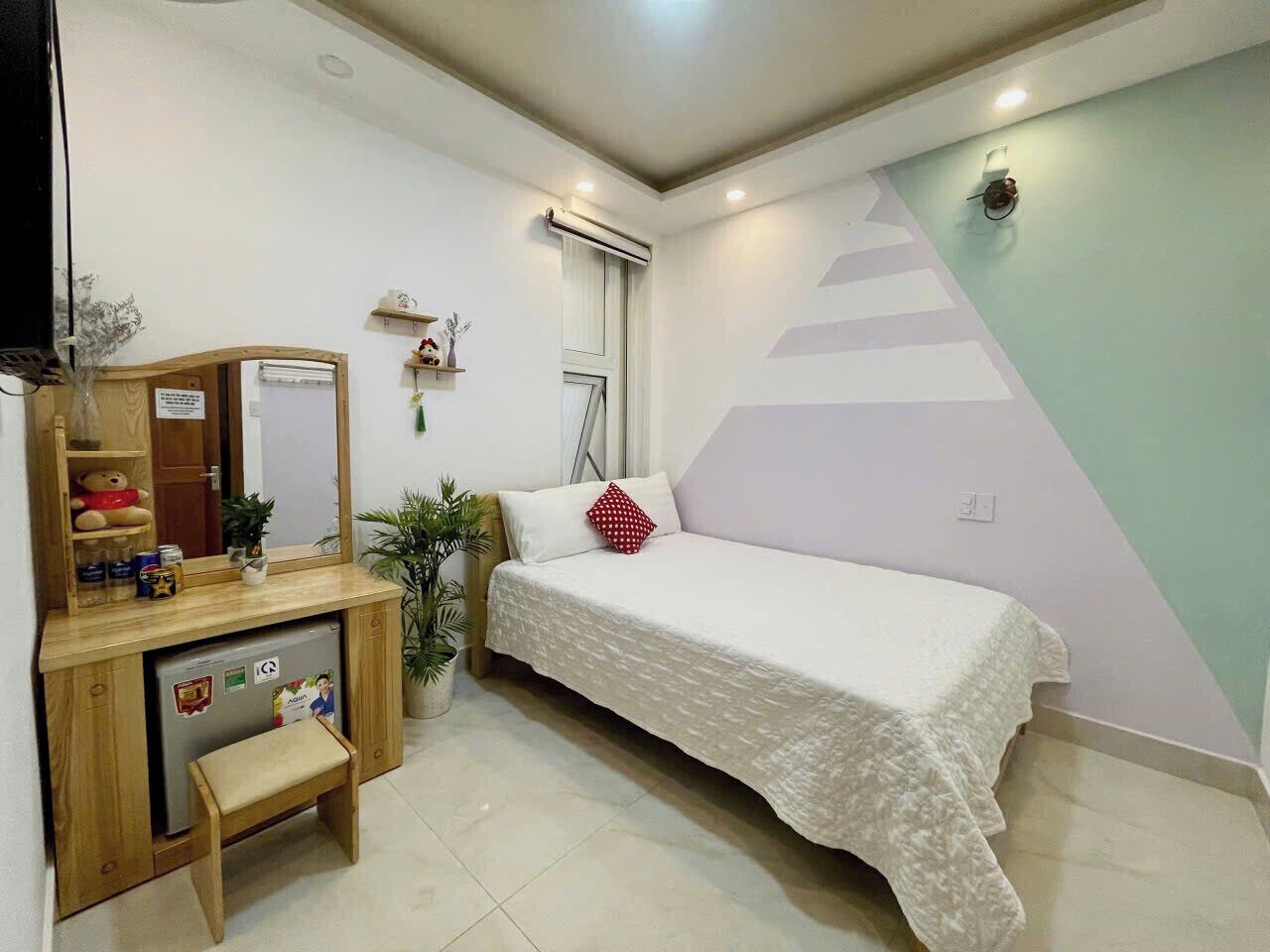 A bedroom with a bed, a desk with a chair, a mirror, a small plant, and a wall-mounted air conditioner.