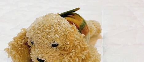 A plush toy dog on a bed with a blue patterned wall in the background.