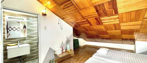 A bedroom with a sloped ceiling, wooden paneling, a bed, a bedside table, a mirror, and a window.