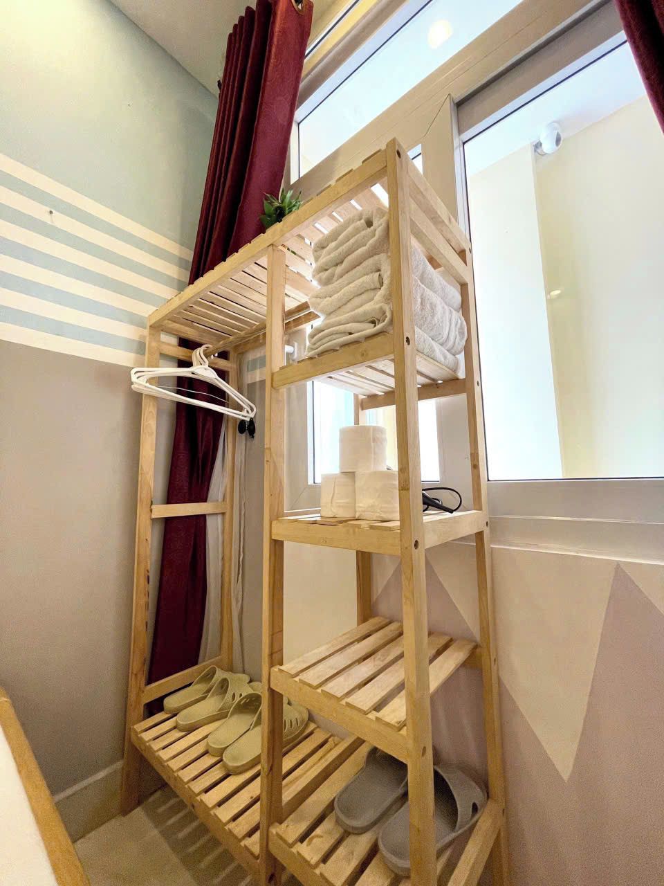 A wooden shelf unit with towels, hangers, and slippers.