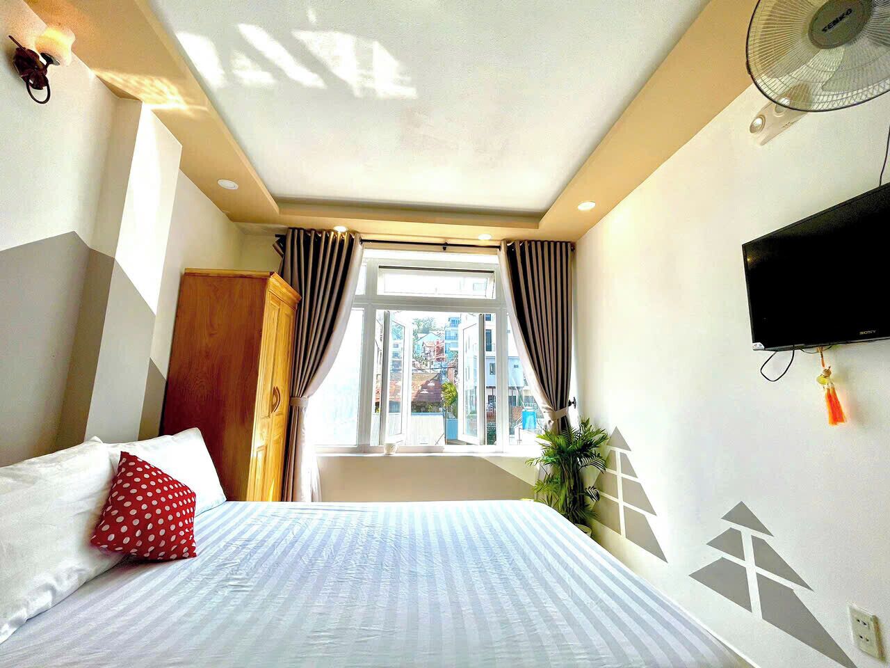 Habitación de hotel con cama, cortinas, televisión y ventana con vistas a edificios.
