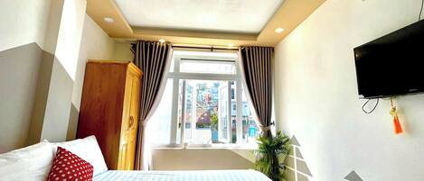 Habitación de hotel con cama, cortinas, televisión y ventana con vistas a edificios.
