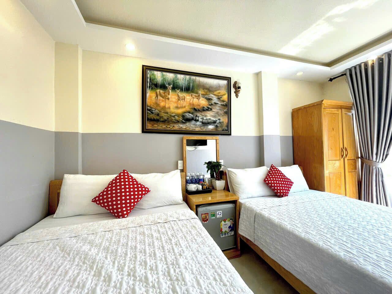 Une chambre d’hôtel avec deux lits, un petit bureau, un réfrigérateur et un tableau au mur.