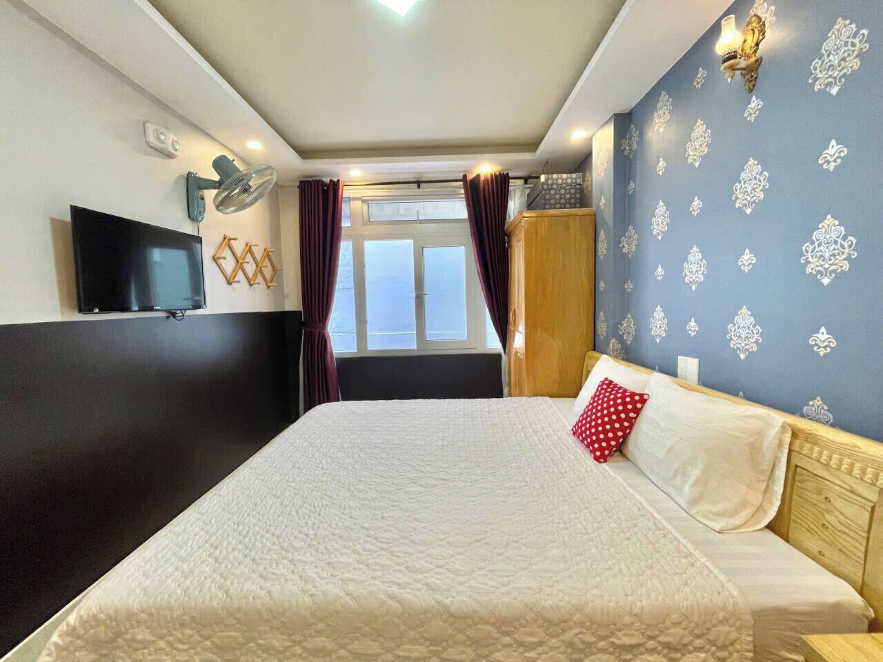 A hotel room with a large bed, a flat-screen TV, a window with curtains, and a decorative wall.