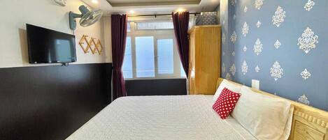 A hotel room with a large bed, a flat-screen TV, a window with curtains, and a decorative wall.