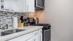 A modern kitchen with white cabinets, a stainless steel sink, a microwave, and a gas stove. - Montrose Chelsea Studio! Medical Center 10 (Houston)