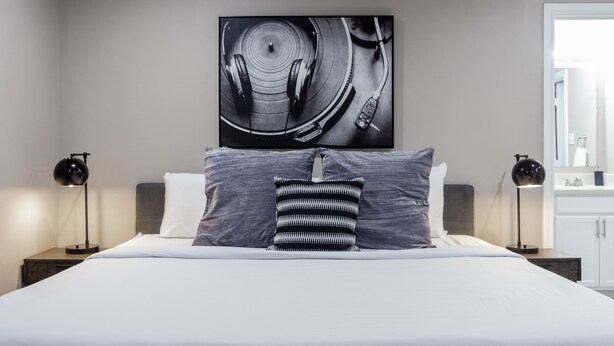 A modern hotel room with a large bed, two bedside tables, a wall-mounted artwork, and a white wardrobe. - Montrose Chelsea Studio! Medical Center 10 (Houston)