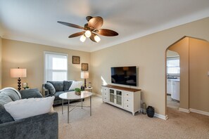 A living room with a ceiling fan, a flat-screen TV, a sofa, a coffee table, and a cabinet. - Quaint Cedar Rapids Home, 4 Mi to Downtown! (Cedar Rapids)