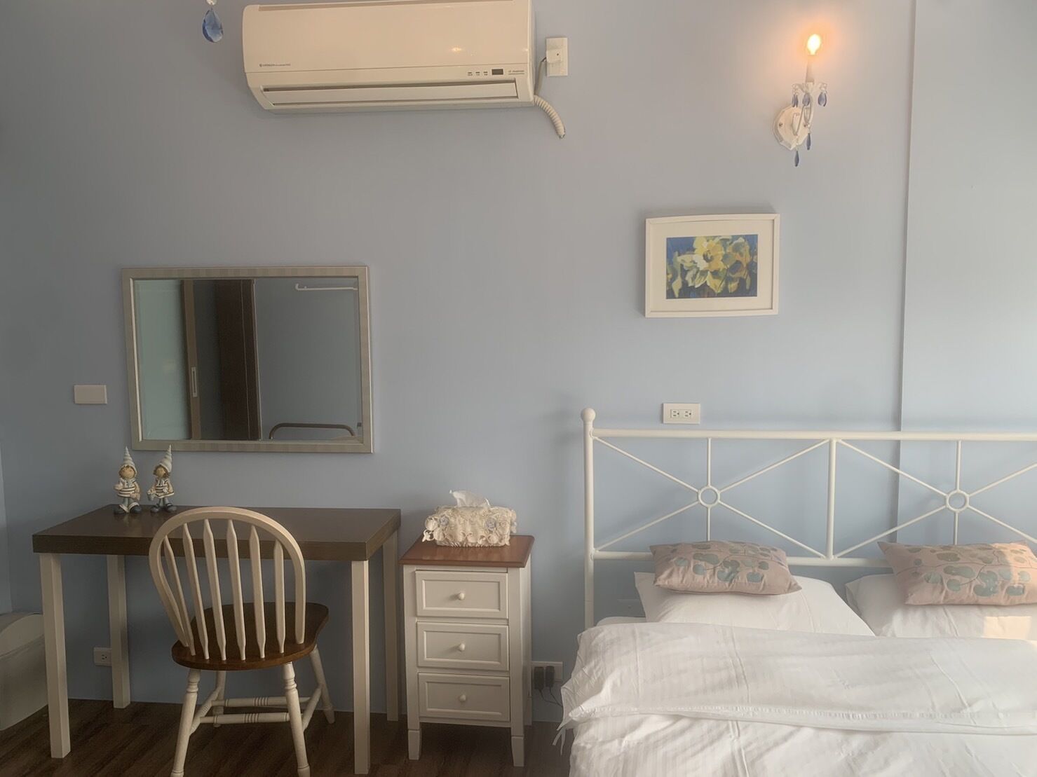 Une chambre à coucher comprenant un lit, un bureau, une chaise, une commode, un miroir et un climatiseur fixé au mur.