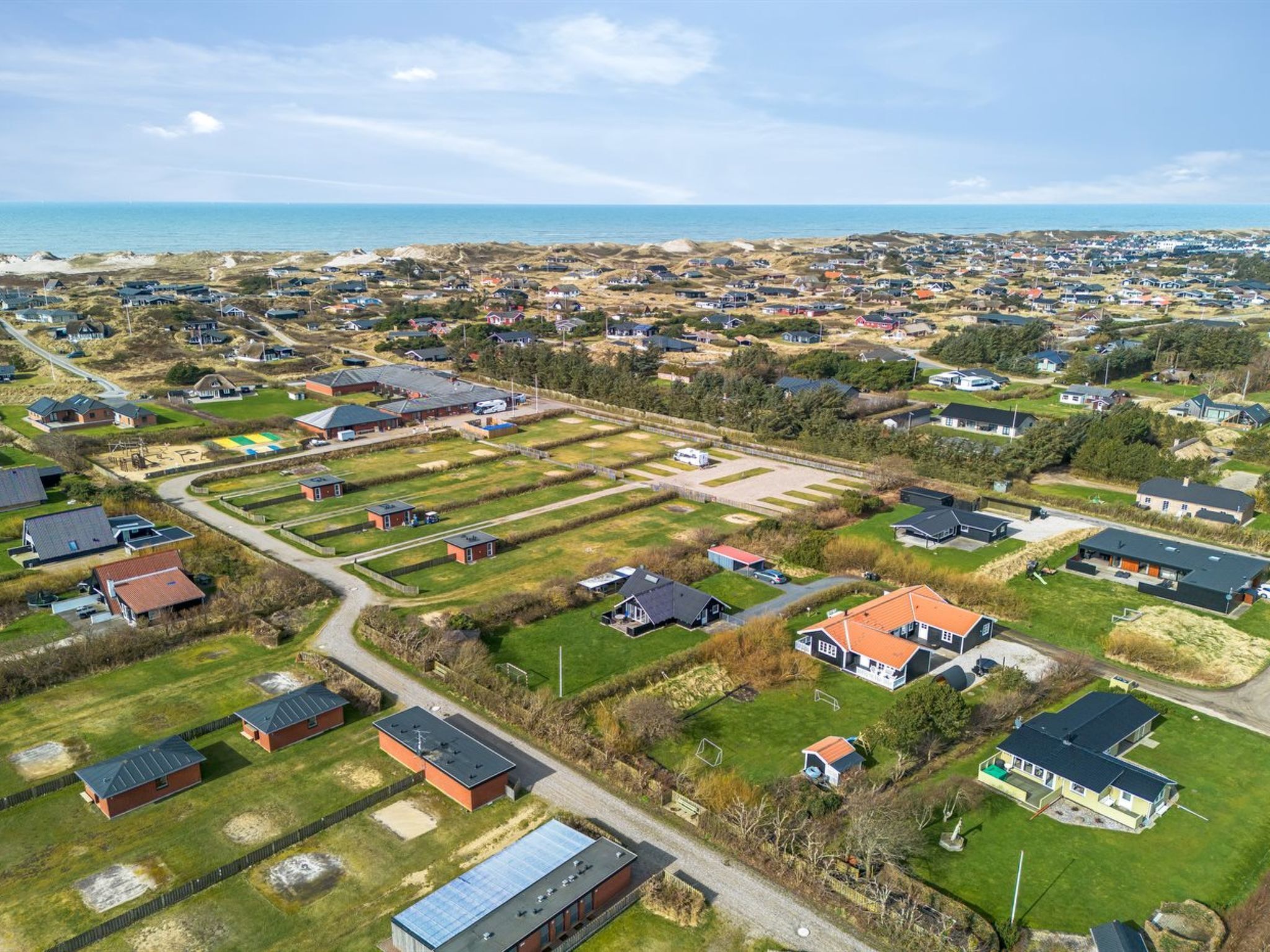 Vue aérienne d’un quartier résidentiel avec des maisons, des espaces verts et une plage en arrière-plan.