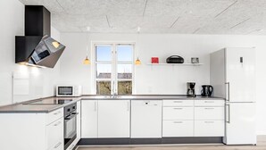 Eine moderne Küche mit weißen Schränken, einer schwarzen Dunstabzugshaube, einer Mikrowelle, einer Kaffeemaschine und einem Kühlschrank.