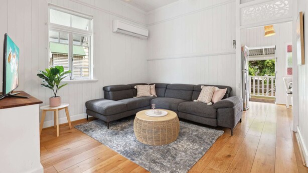 A living room with a grey sectional sofa, a round coffee table, a potted plant, a painting, and a ceiling fan. - Tranquil 3-Bed Family Home with Spacious Backyard (Nundah)
