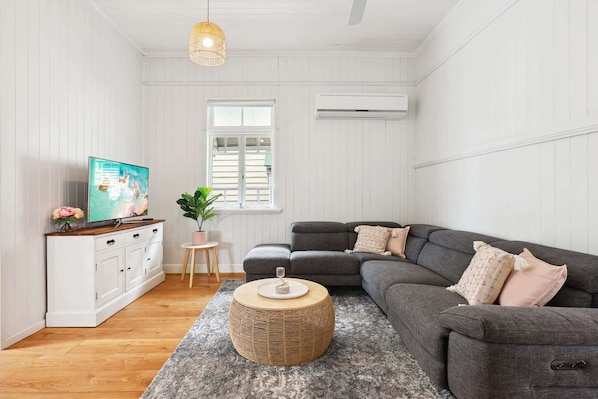 A living room with a grey sofa, a TV, a small table with a plant, and a wicker ottoman.