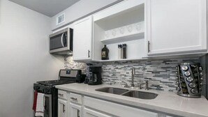 A modern kitchen with white cabinets, a stainless steel sink, a microwave, a coffee maker, and a stove.