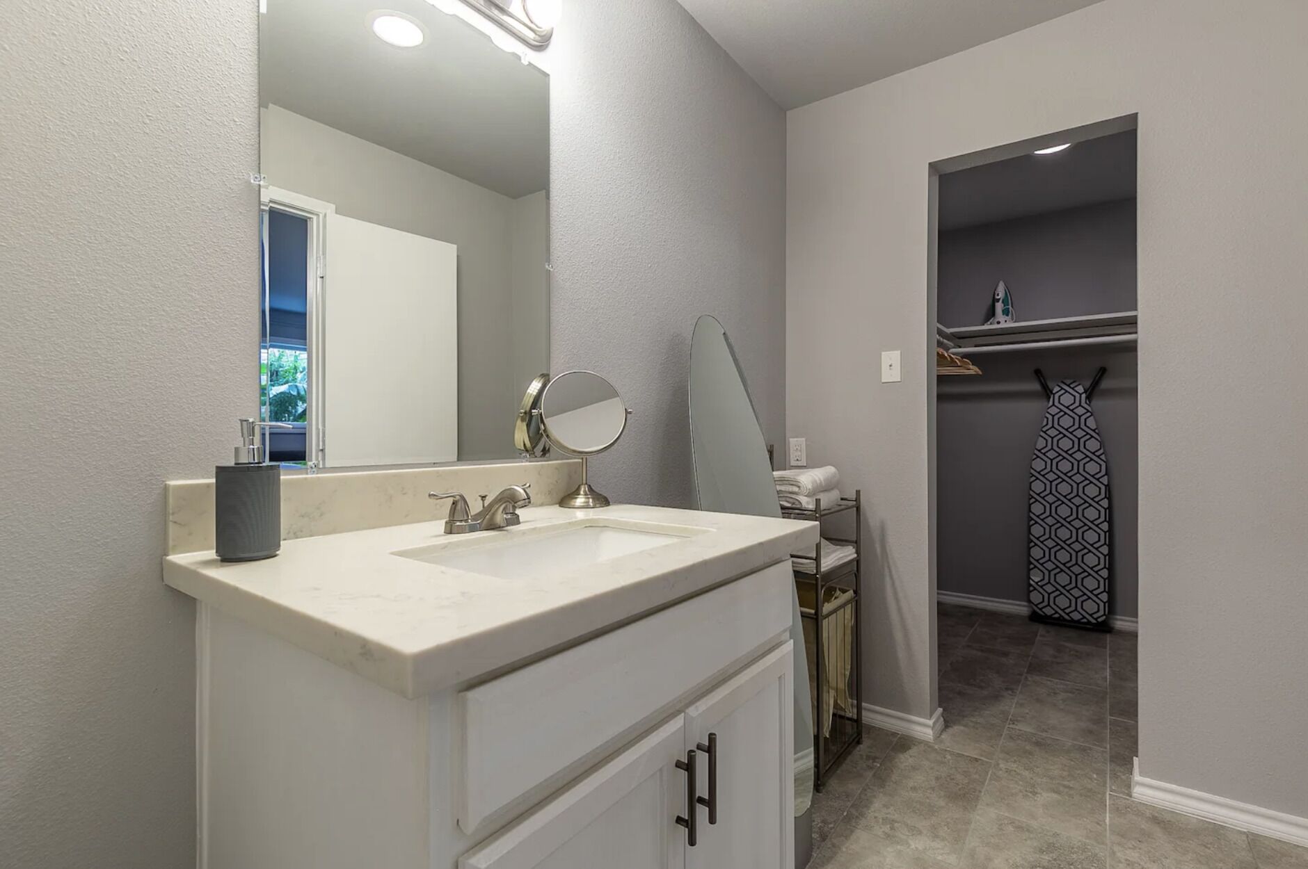 Une salle de bain avec un meuble-lavabo blanc, un miroir rond et un porte-serviettes.