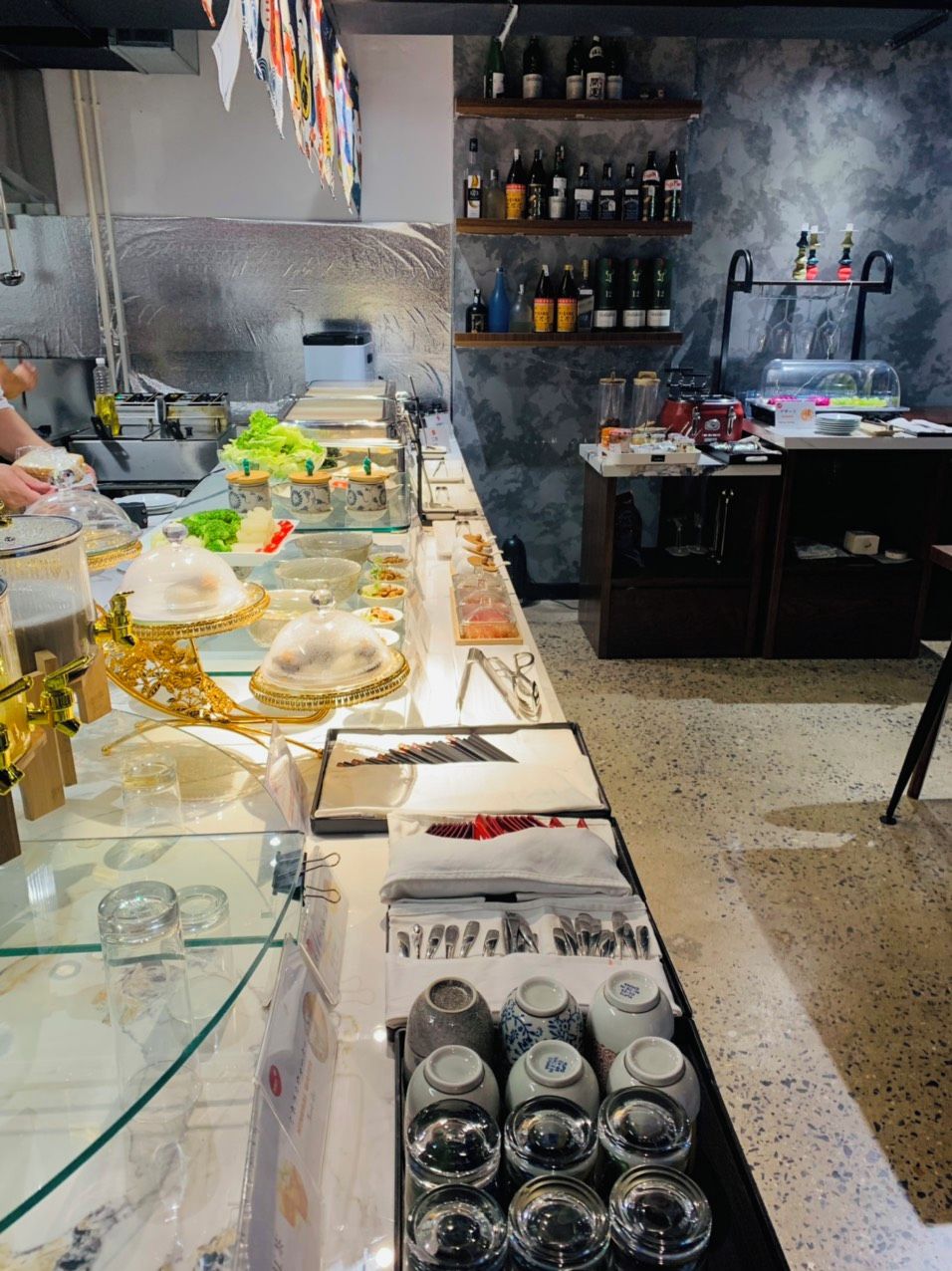 A buffet setup with a variety of food items, a wine selection on shelves, and a kitchen area in the background.