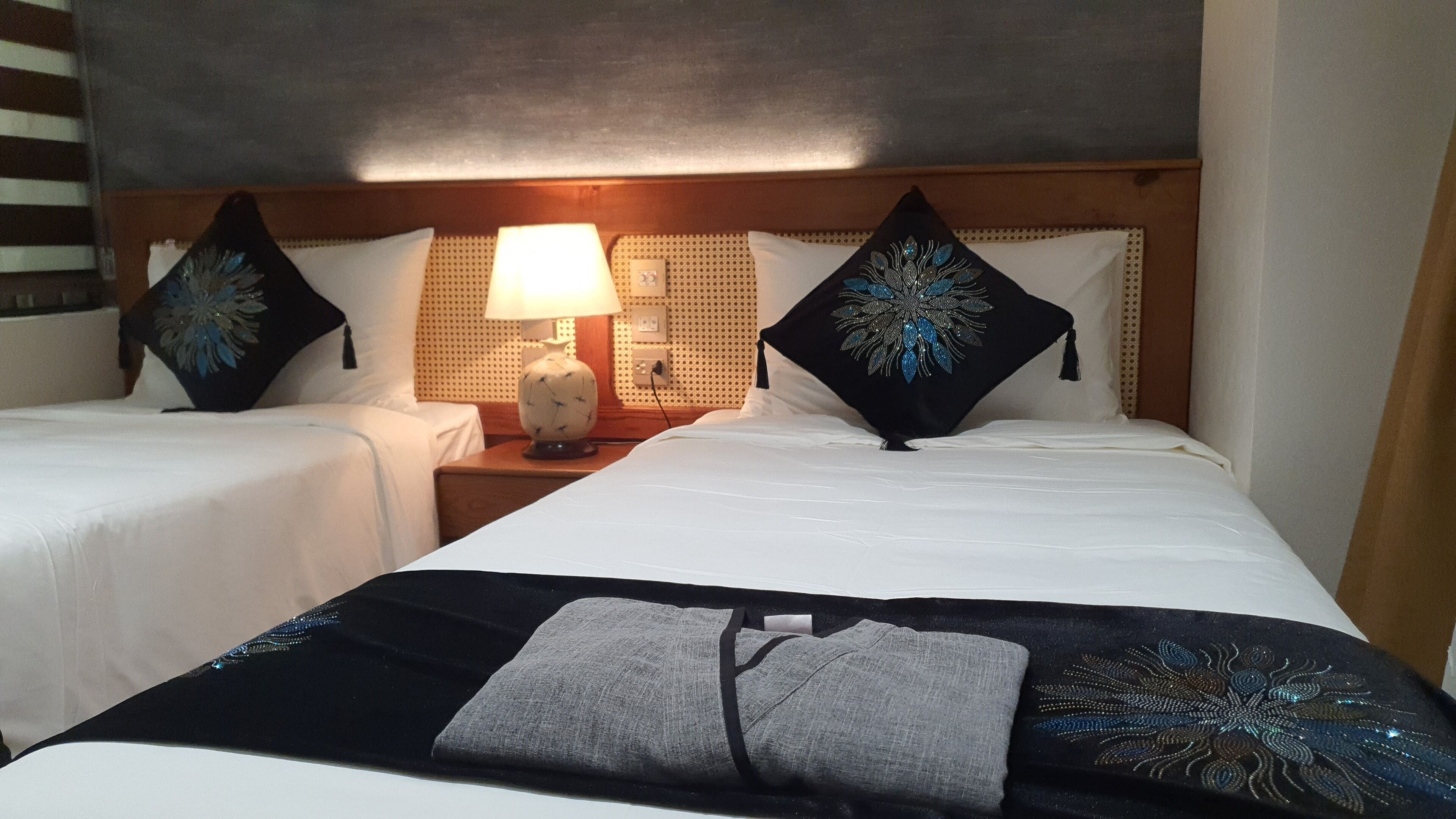 Une chambre d’hôtel avec deux lits simples, une table de chevet avec une lampe et des coussins décoratifs.
