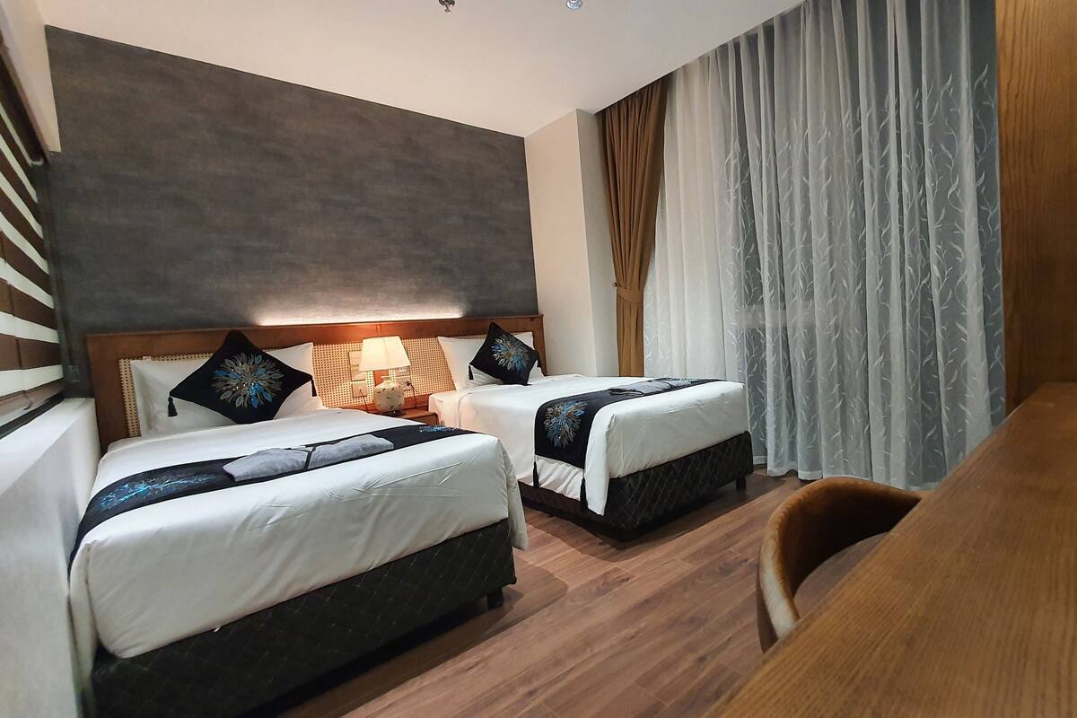 Habitación de hotel con dos camas, un escritorio de madera y una silla.