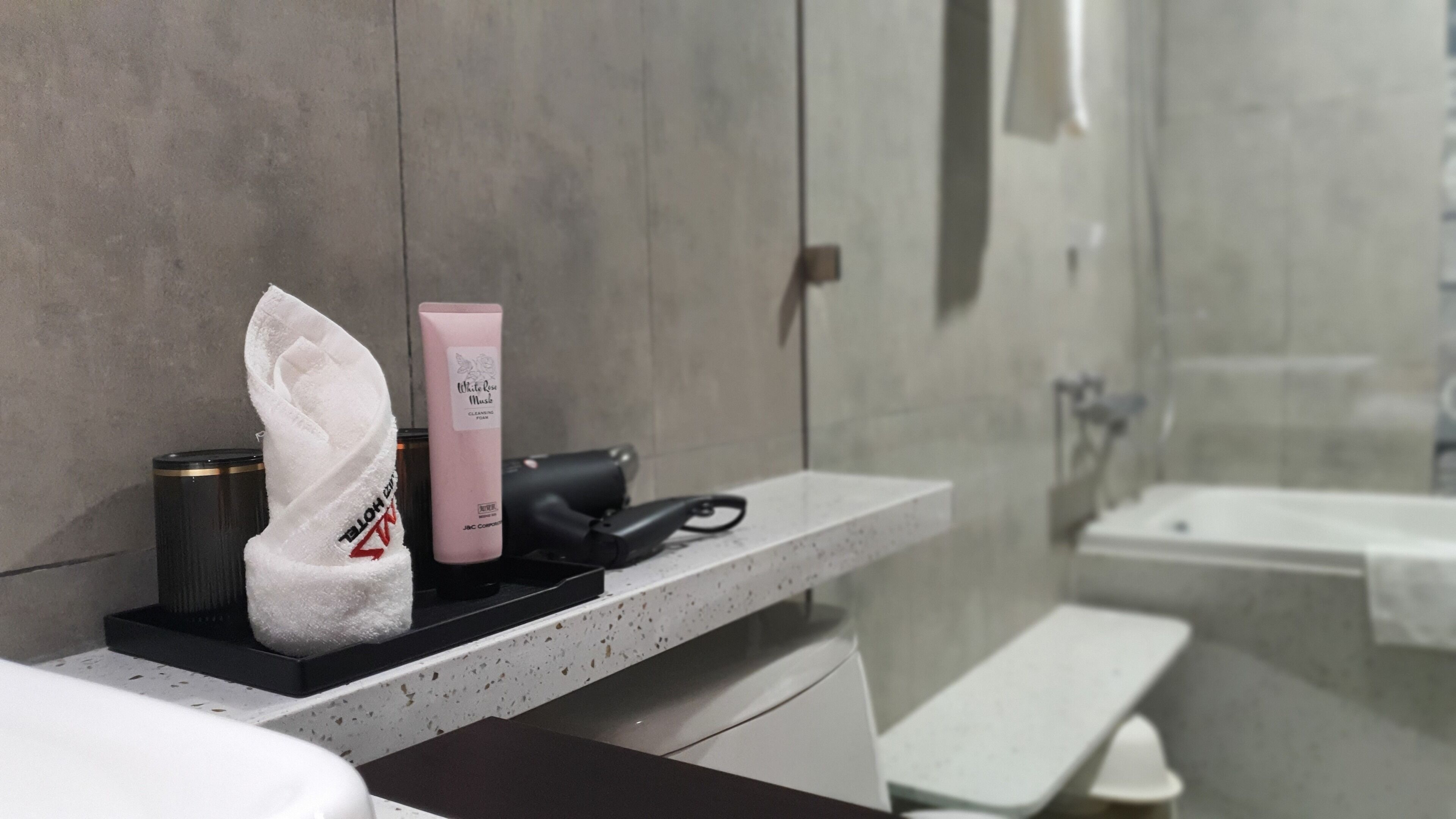Un baño con una encimera que sostiene una toalla, una botella rosa y un secador de pelo negro.